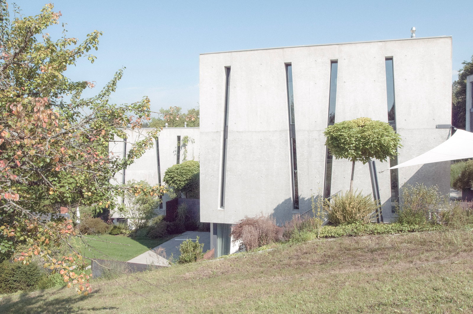 Betonhaus mit Fensterschlitzen und Sonnensegel in der Siedlung like2live
